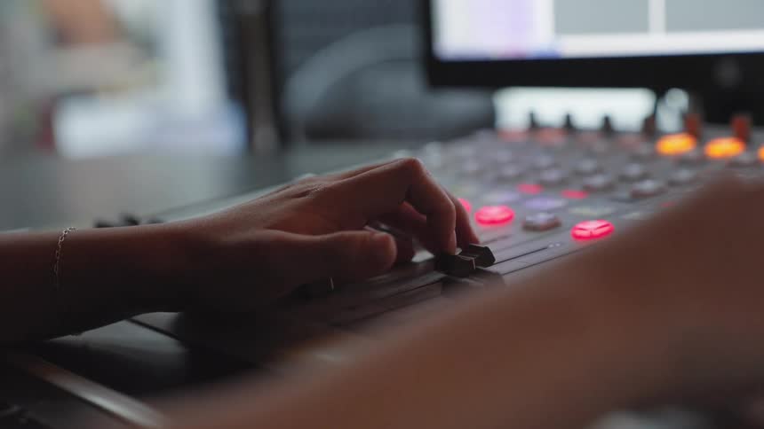 A close-up of a person's hands adjusting sliders on a professional audio mixing console in a studio