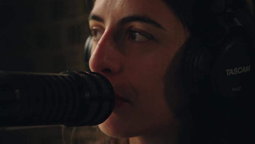 An intimate close-up of a female singer emotionally recording a track in a dark studio