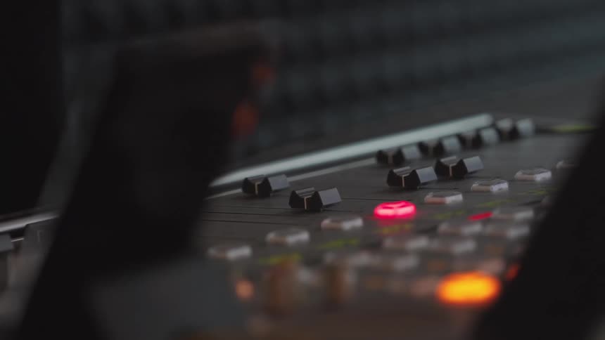 An audio engineer's hand adjusts faders and presses glowing red buttons on a professional mixing console