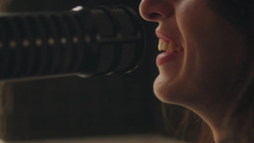 Extreme close-up of a woman's mouth as she speaks into a broadcast microphone in a recording studio