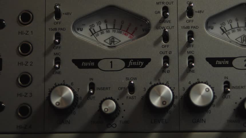 Close up of a sound engineer's hand adjusting the knobs and switches on a vintage-style audio preamp in a recording studio