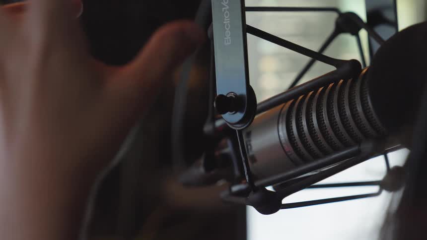 A close-up of a hand adjusting a professional studio microphone and gesturing during a recording session