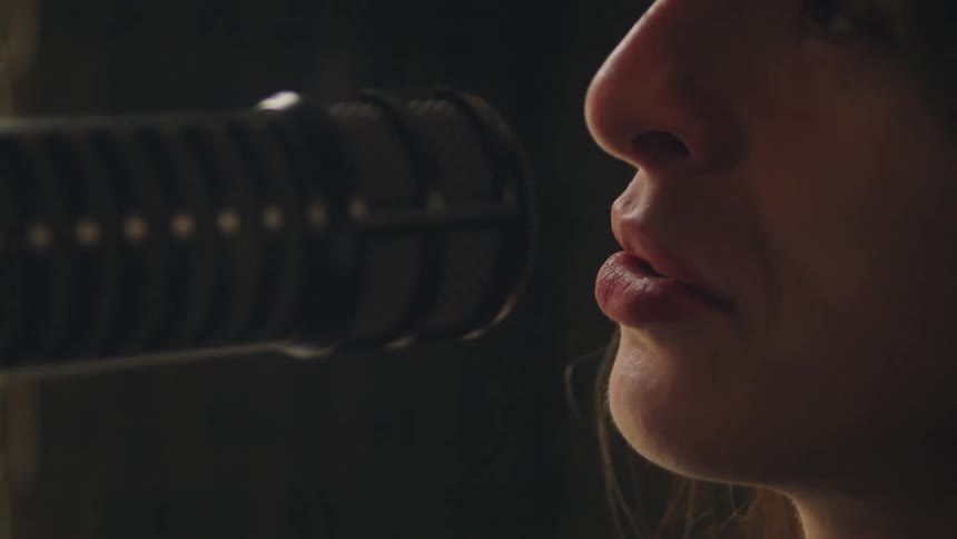 Close-up profile of a woman's lips and nose as she speaks into a studio microphone