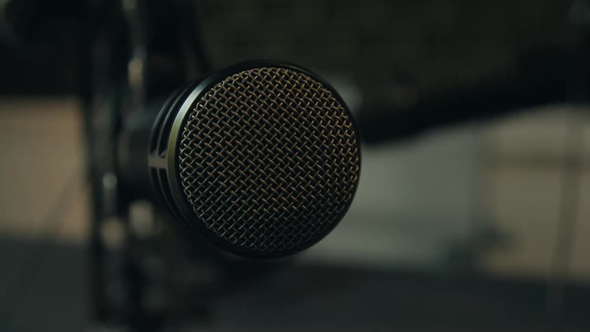 A close-up shot of a professional recording microphone slowly pans into frame in a dimly lit studio