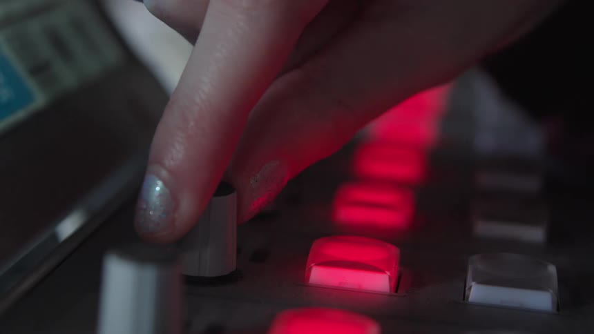 A close-up of a music producer's hand with glittery nails turning a knob and pressing glowing red buttons on a beat machine