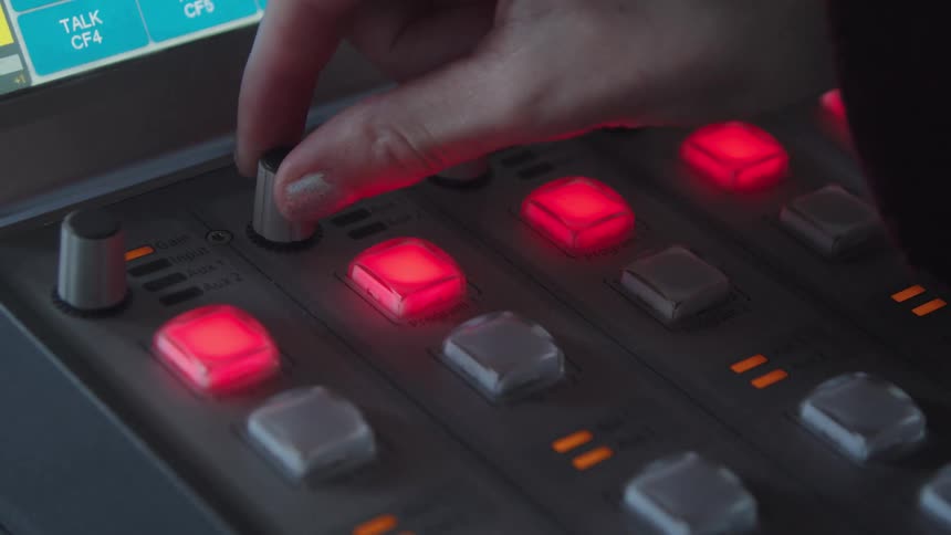 A sound engineer's hand adjusts a dial on a professional audio mixing console with glowing red buttons