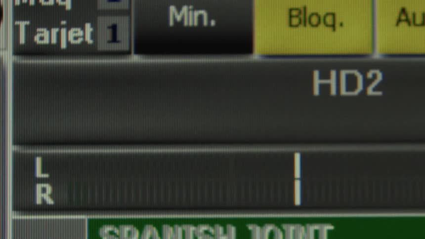 A close-up of a digital audio stereo level meter with green bars fluctuating on a professional mixing console