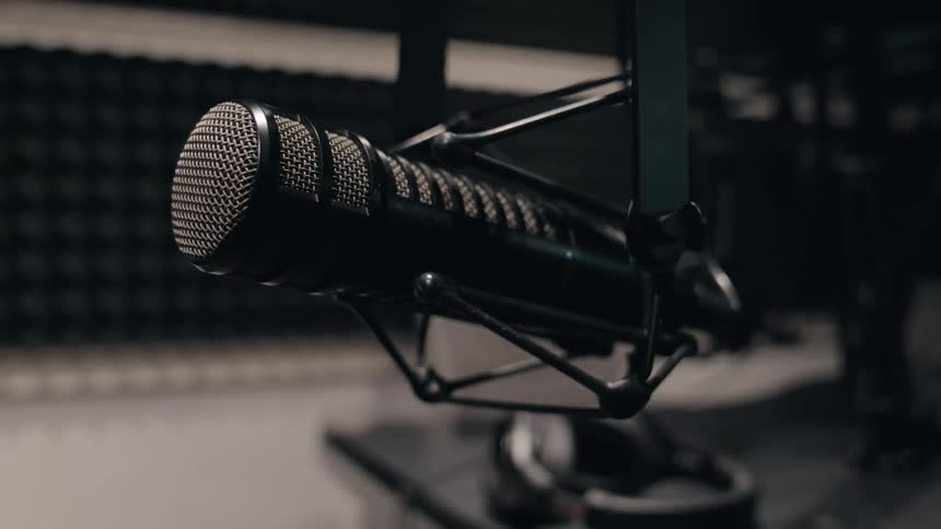 Close-up shot of a professional microphone suspended in a shock mount in a dark, soundproof recording studio