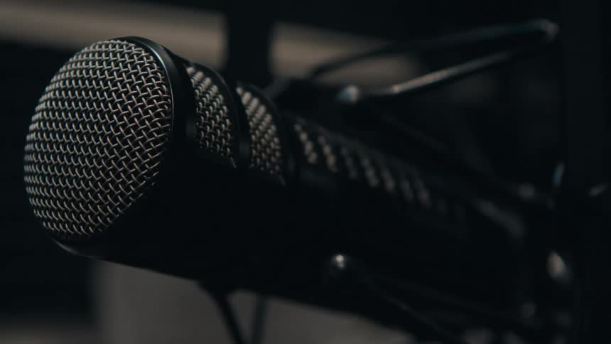 A dramatic close-up of a professional broadcast microphone as the focus shifts in a dark studio