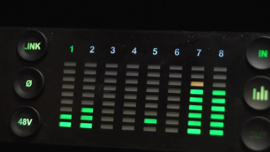 Close-up of a digital audio interface's multi-channel LED level meters fluctuating in a recording studio