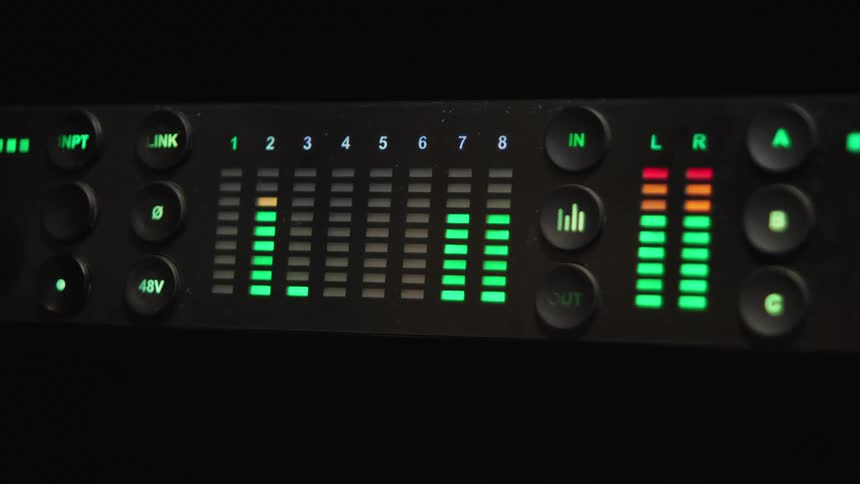 Close-up of a digital audio interface with green LED level meters fluctuating in a dark recording studio