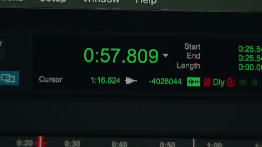 A close-up of a bright green digital timecode counting up quickly on a dark computer screen during the editing process