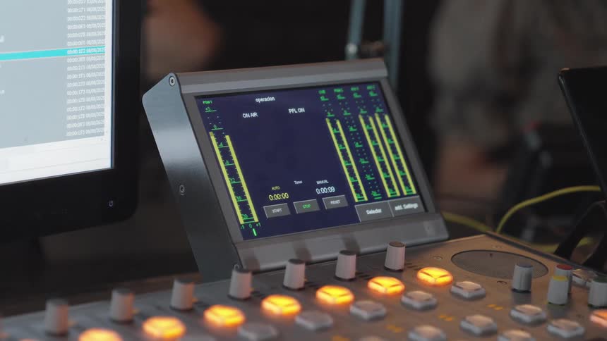 Close-up of a digital audio mixing console with active sound level meters and glowing buttons in a recording studio