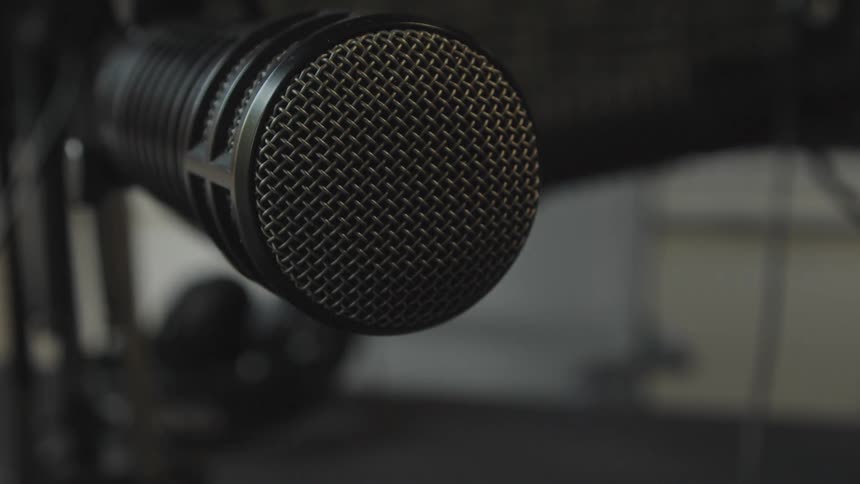 A dramatic rack focus close-up on a professional studio microphone ready for broadcast