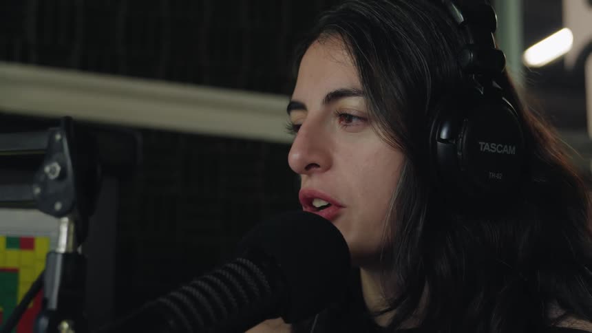 A close-up profile of a woman with headphones speaking into a professional microphone in a recording studio