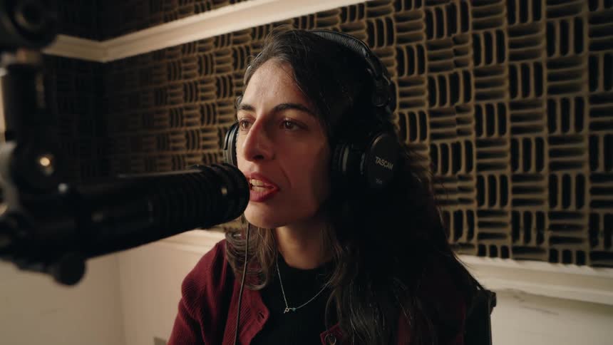 A female singer with headphones on sings passionately into a professional microphone in a soundproofed recording studio