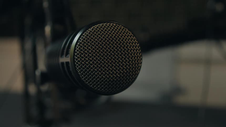 A hand adjusts a professional dynamic broadcast microphone in a dimly lit recording studio