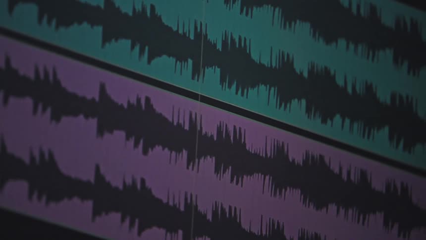 A close-up of colorful audio waveforms playing back on a timeline in digital editing software