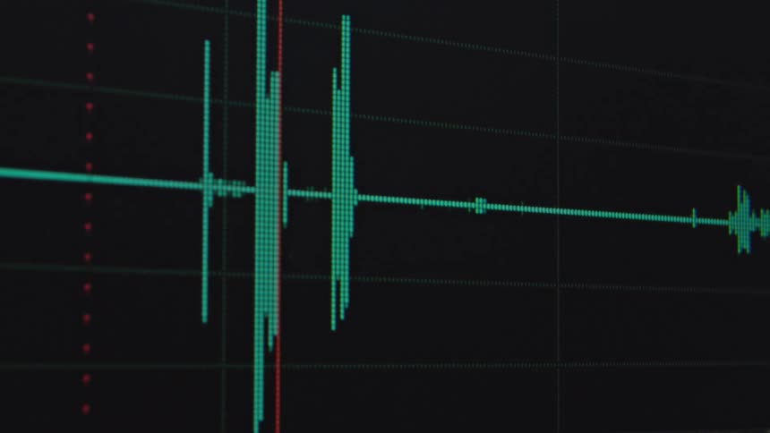 Close-up of a green audio waveform on a digital timeline with a red playhead scrolling across