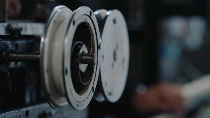 Close-up on an industrial machine with a spinning spool winding white thread in a manufacturing factory