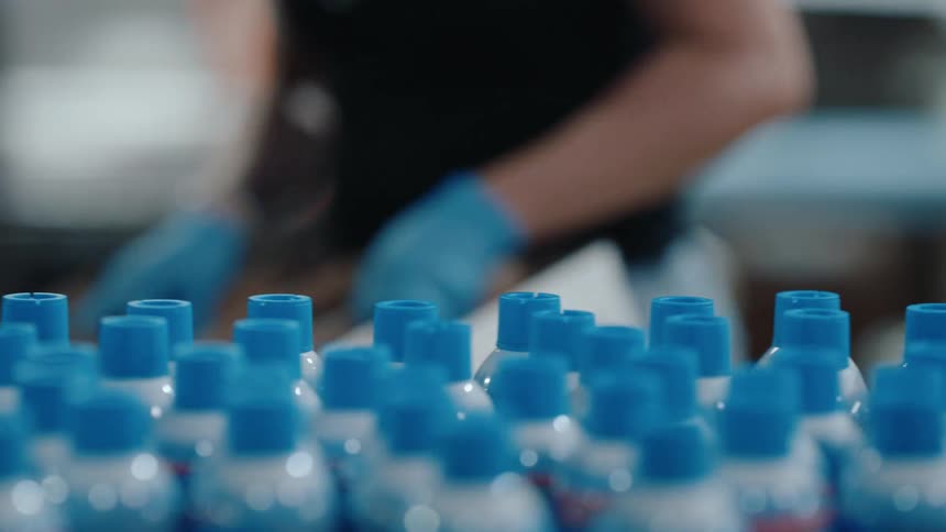 A factory worker packs bottles with blue caps on a manufacturing assembly line