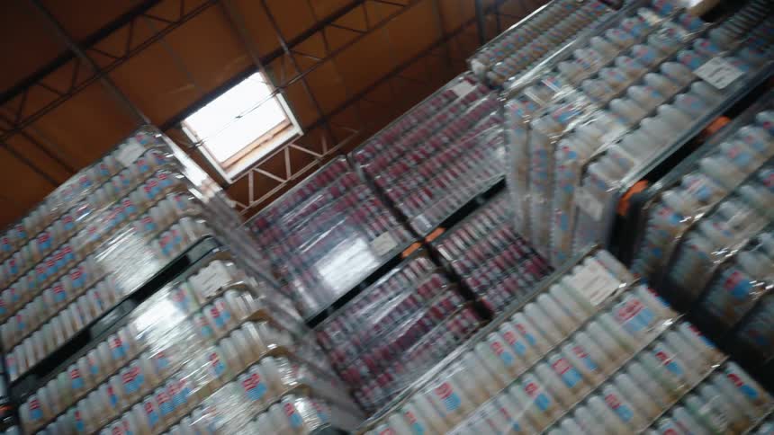 Low-angle rotating shot pulling back from massive stacks of canned beverages in a large warehouse