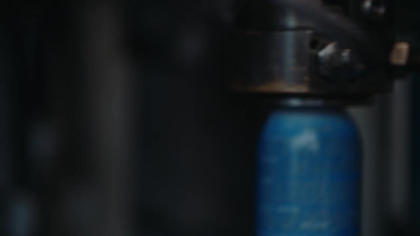 Close-up of an automated machine filling aerosol spray cans on a factory production line