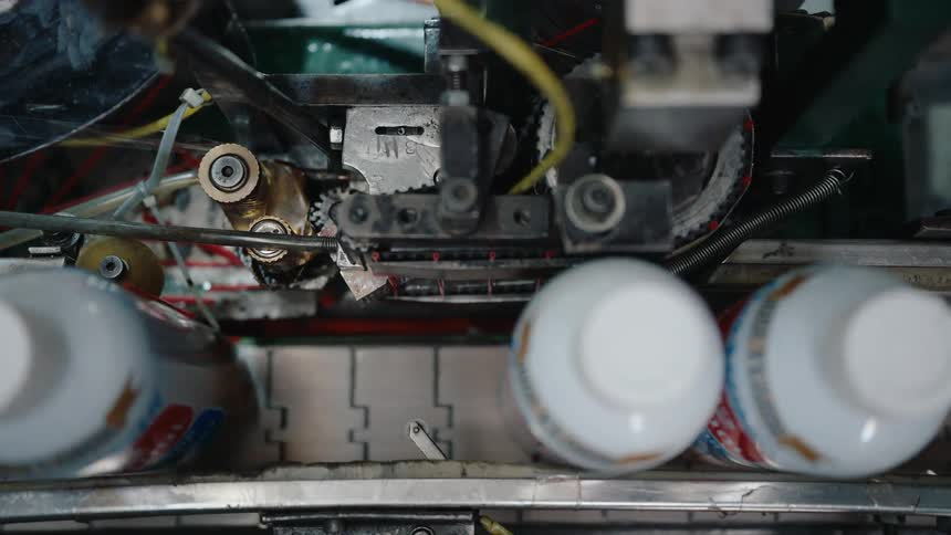 Overhead view of an automated industrial machine processing cans on a factory assembly line
