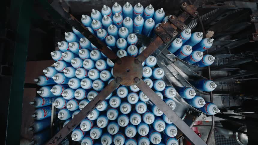 Overhead shot of an industrial machine holding dozens of blue aerosol spray cans in a circular pattern