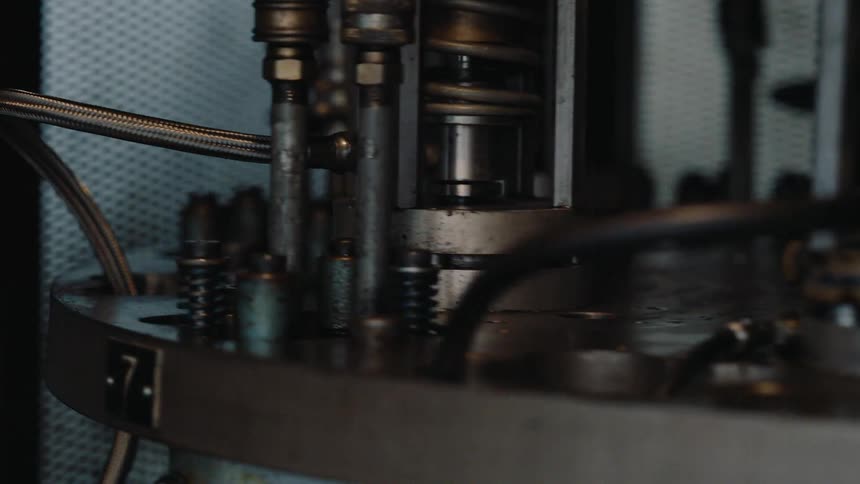 A detailed close-up shot captures the complex, automated movements of a vintage industrial rotating machine in a factory setting