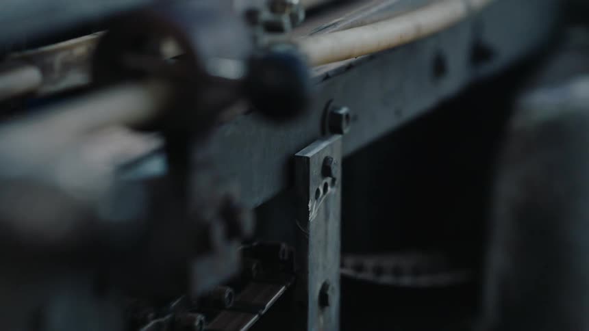 A rusty chain on an old industrial machine moves slowly in a dimly lit factory