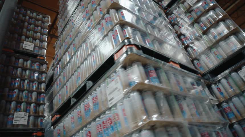 Low-angle rotating shot of massive stacks of beer cans wrapped on pallets in a brewery warehouse