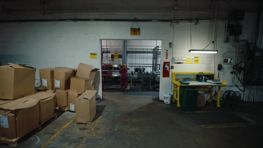 Wide, static view of an industrial warehouse interior with a worker on a distant production line