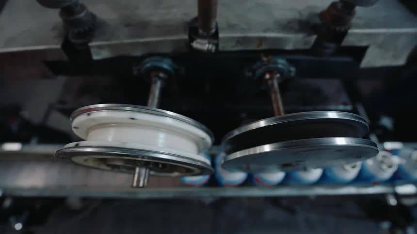 A close-up view from above shows industrial machinery with rotating parts processing aerosol cans on a factory production line