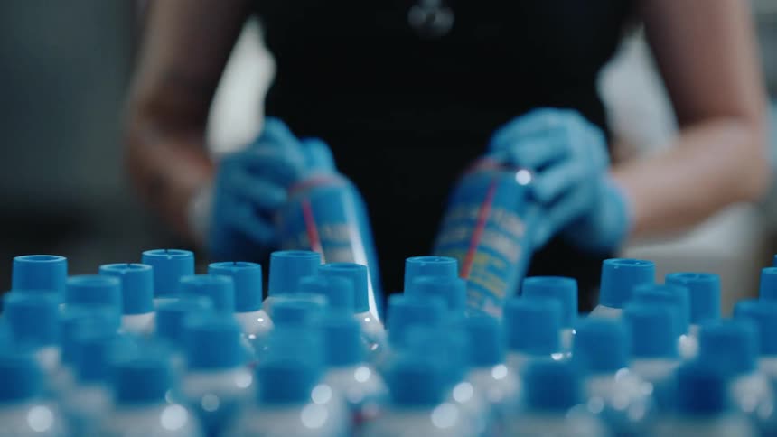 Slow motion close-up of a factory worker inspecting and arranging aerosol cans on a production line