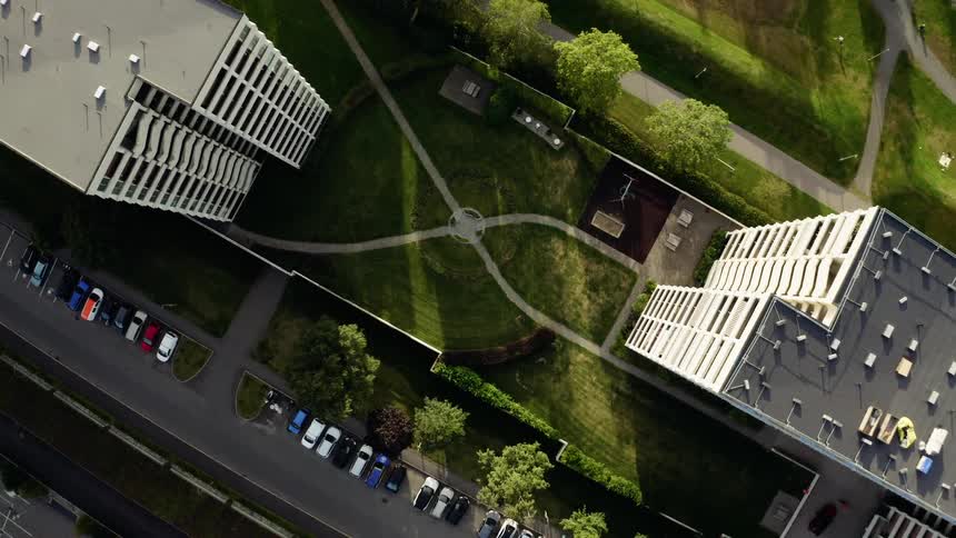 Slowly descending top-down aerial shot of a modern residential complex courtyard with a playground and symmetrical green lawn