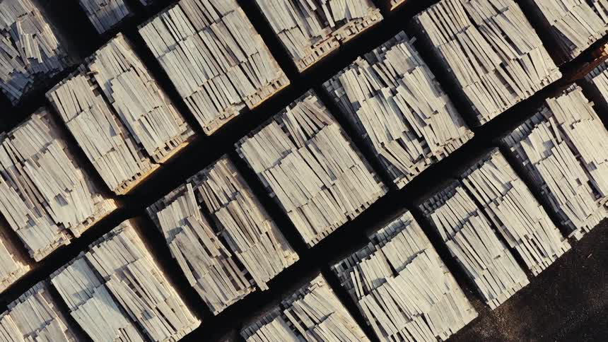 A slow aerial top-down zoom out reveals rows of neatly stacked wooden planks and lumber at a sawmill