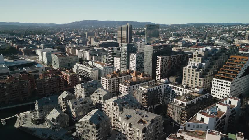 Aerial view of a city construction site tilts up to reveal a modern urban skyline with unique architecture on a sunny day