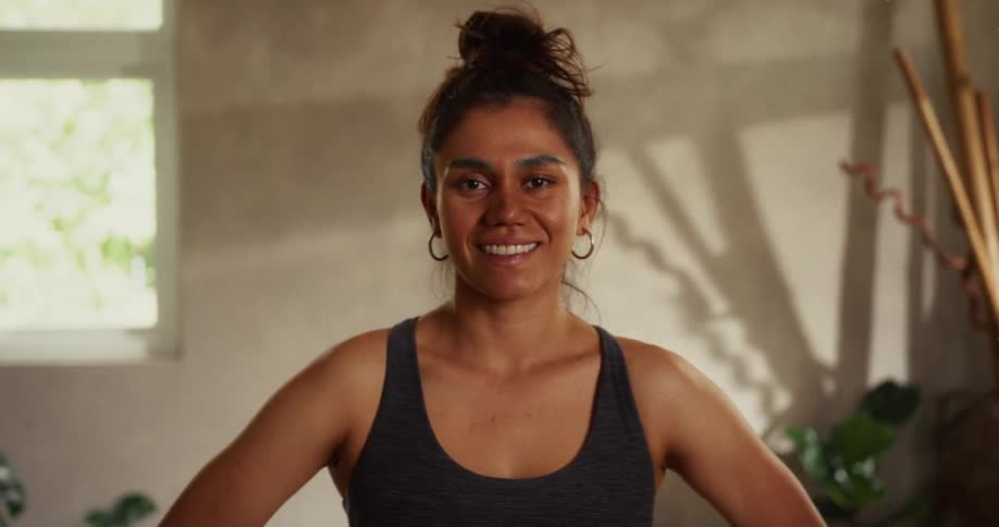Close-up portrait of a confident woman in workout attire smiling warmly in a sunlit room