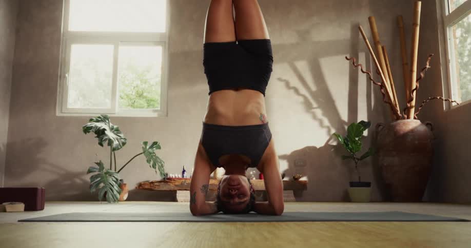 A focused woman holds a perfect yoga headstand in a serene and sunlit studio
