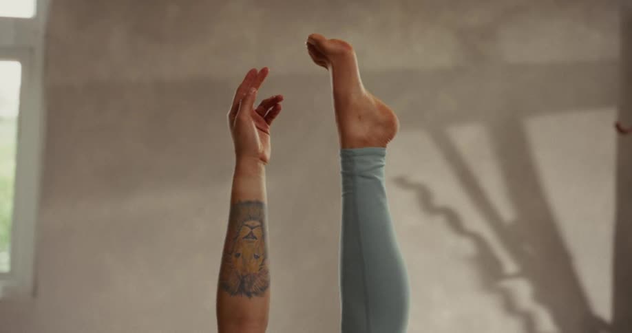 A close-up of a tattooed arm and a leg in leggings holding a graceful balance pose during a yoga session