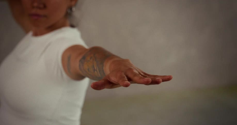 Close up detail of a woman's hand and tattooed arm extended during a warrior yoga pose