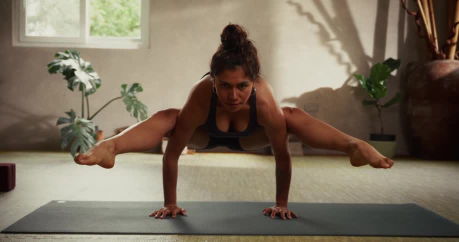 A strong and focused woman performs the advanced Firefly yoga pose (Tittibhasana) in a serene, sunlit studio