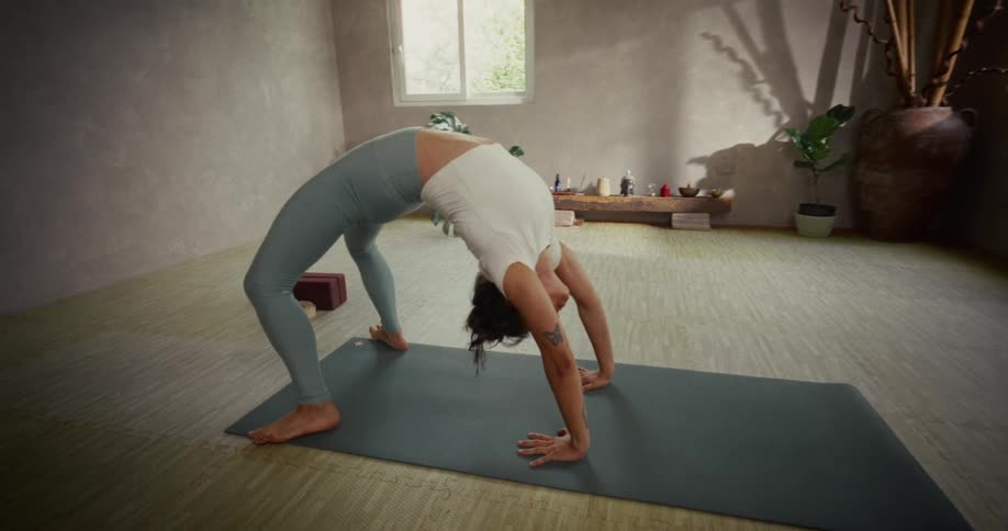 A flexible woman gracefully performs a backward bend into a wheel pose on her yoga mat in a tranquil studio