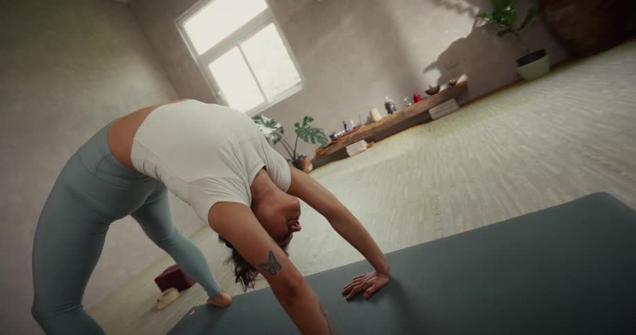 A woman gracefully flows through a challenging yoga sequence in slow motion in a serene, sunlit studio
