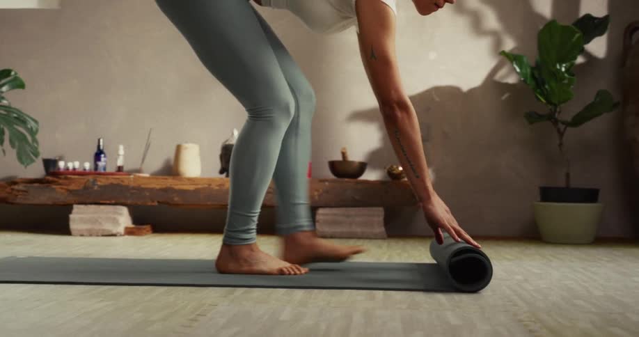 A woman in leggings unrolls her yoga mat in a tranquil studio in slow motion, preparing for her practice