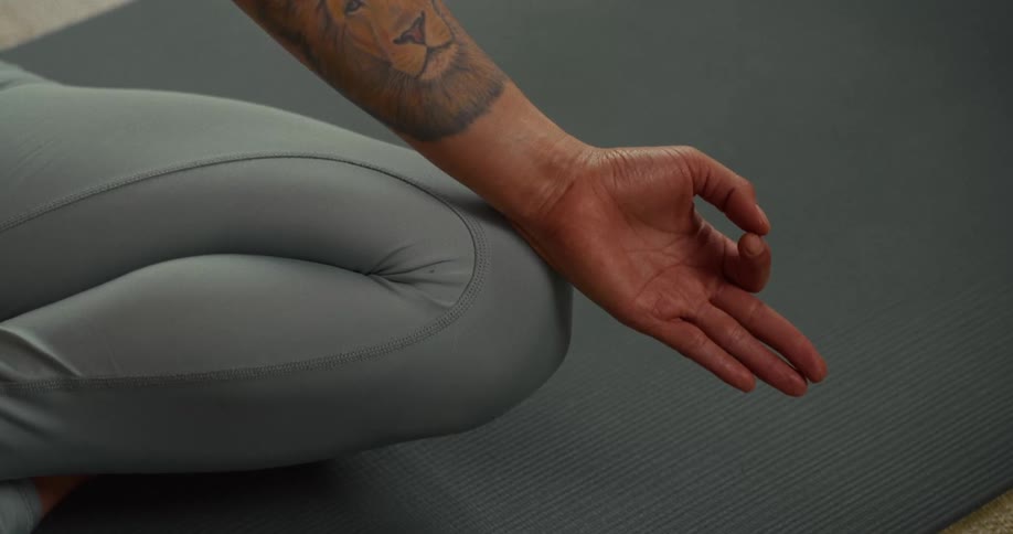 Close up of a person's hand in a yoga mudra pose while sitting on a mat for meditation