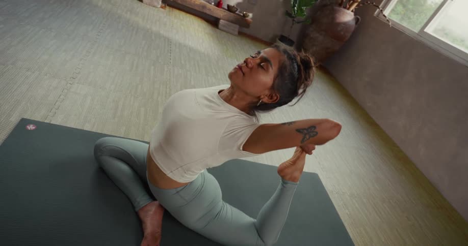 A flexible woman performs a deep backbend, holding the one-legged king pigeon yoga pose on a mat in a serene studio