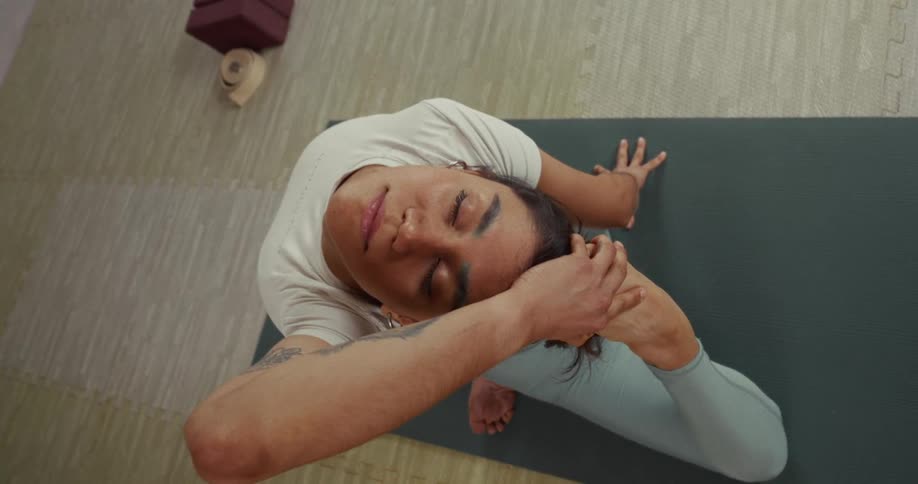 A serene woman with eyes closed performs a deep One-Legged King Pigeon yoga pose, seen from a high angle