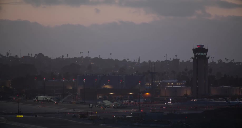 Time-lapse of an air traffic control tower overlooking a bustling airport tarmac during a hazy twilight